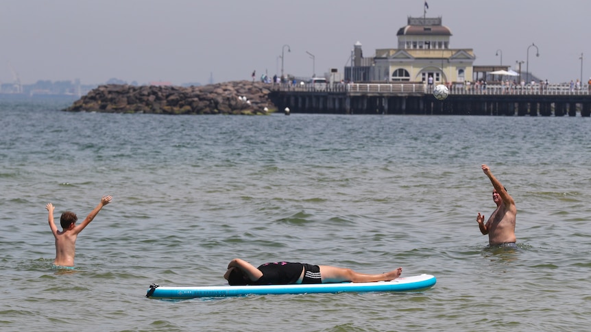 a man and two children in the water, as one of the children lies on a sufboard