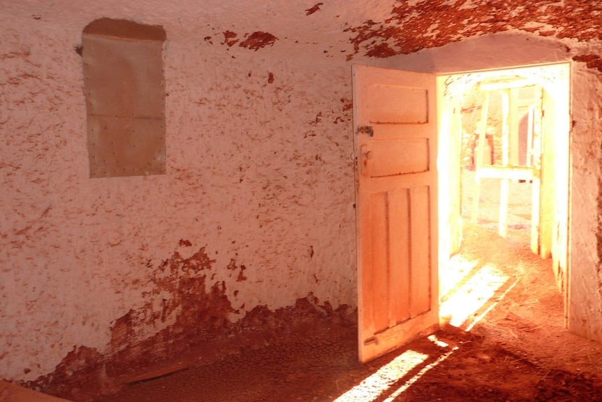 The interior of a Coober Pedy dugout with the front door open and sunlight streaming through the threshold