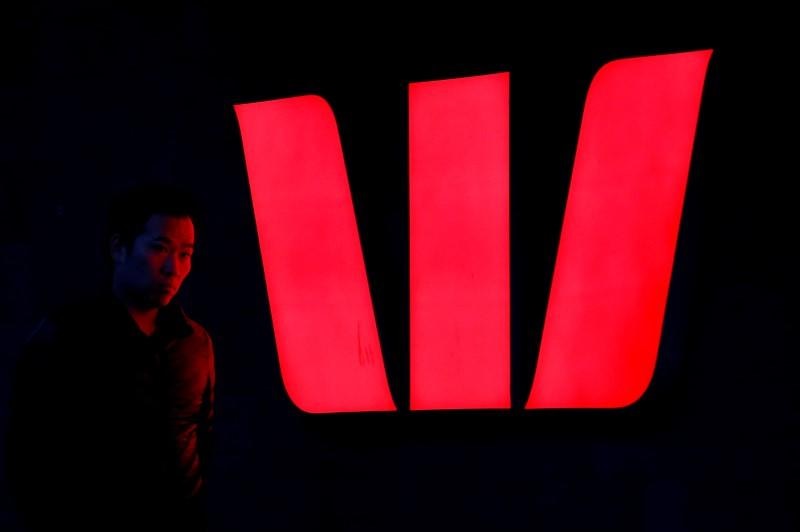 A man walks past an illuminated logo for Australia's Westpac Bank in Sydney