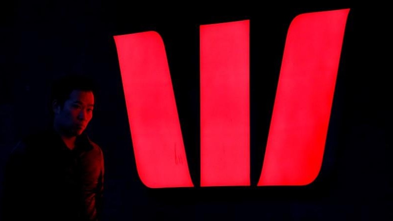 A man walks past an illuminated logo for Australia's Westpac Bank in Sydney