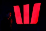 A man walks past an illuminated logo for Australia's Westpac Bank in Sydney