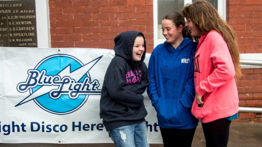 Three girls huddle next to a sign reading 'Blue Light Disco'