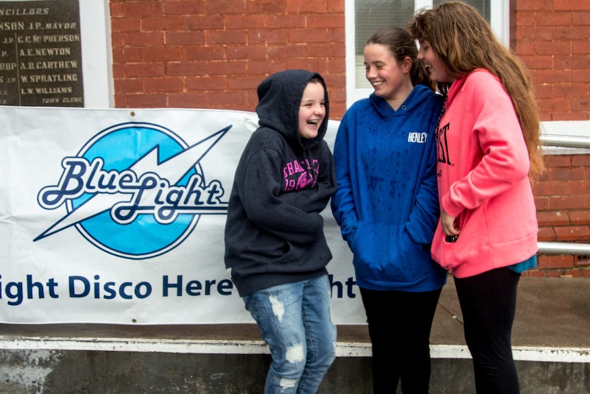 Three girls huddle next to a sign reading 'Blue Light Disco'