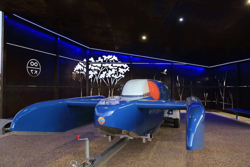 A blue speed boat on a trailer inside a shelter.