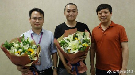 Fu Guo, centre, holds a bouquet and stands in between two men.
