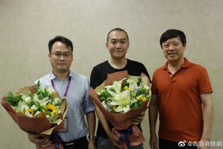 Fu Guo, centre, holds a bouquet and stands in between two men.