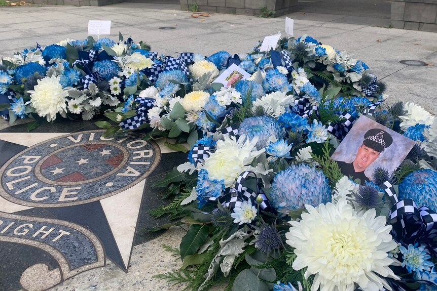 A row of blue and white flowers and photographs are laid out above a Victoria Police marble floor.