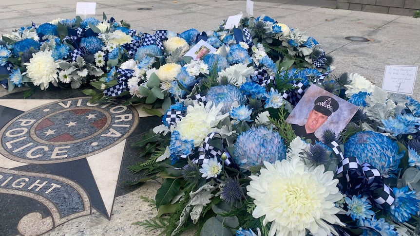 A row of blue and white flowers and photographs are laid out above a Victoria Police marble floor.