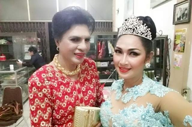 Mommy Yuli wears a red dress, next to a friend who is wearing a blue formal dress and a tiara.