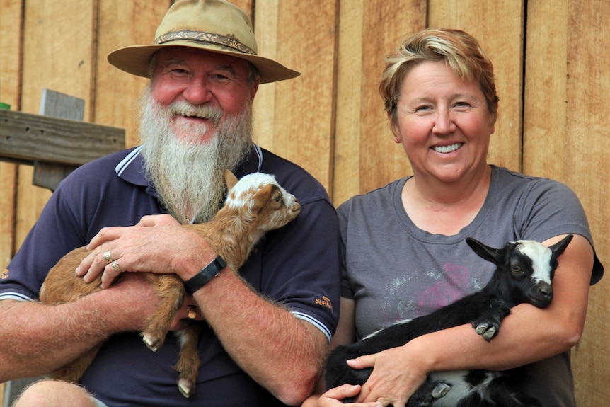 A man and woman sitting and holding young goats