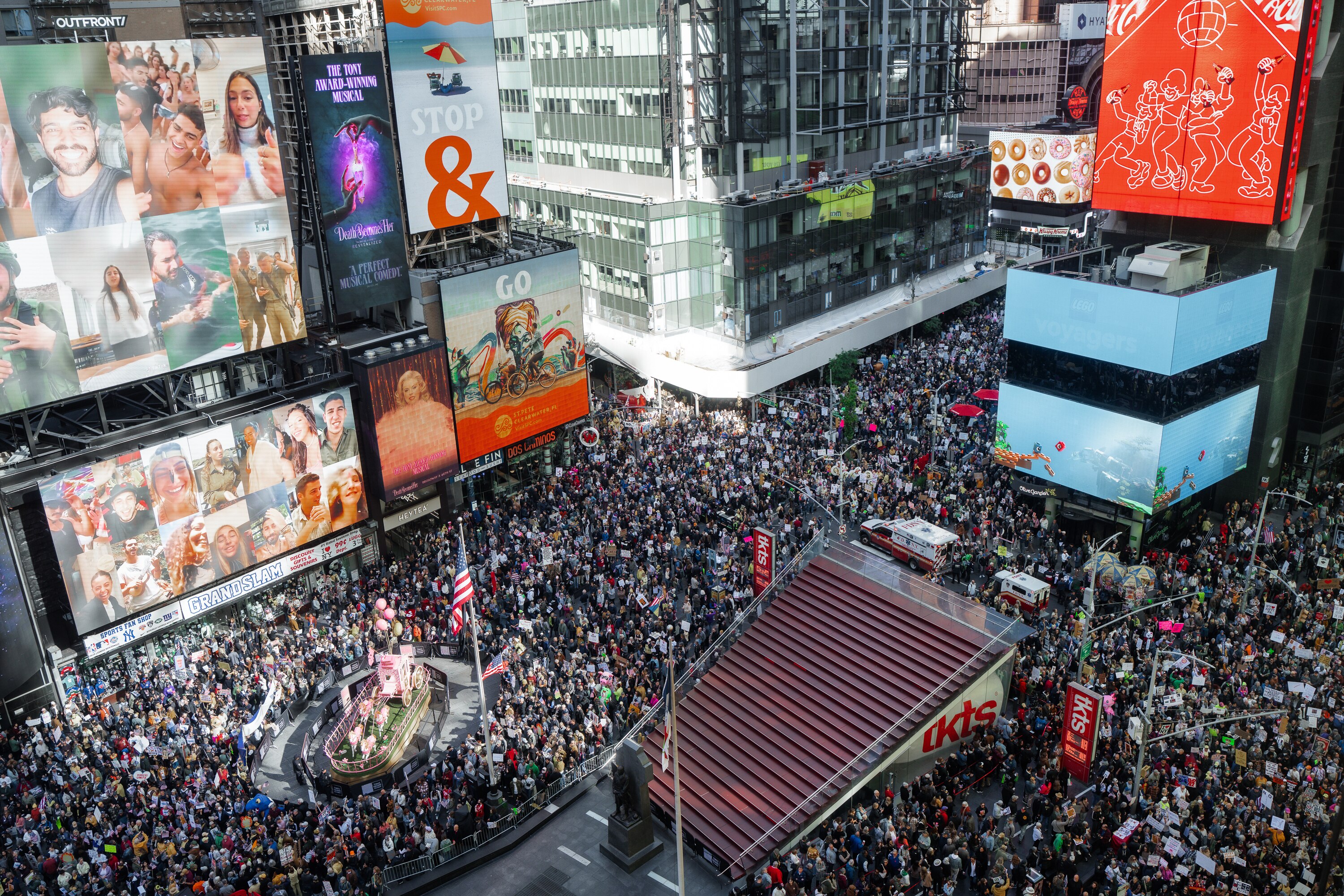 Times Square packed with large crowds of protesters, shot fom above to show the square's billboard signs and red steps
