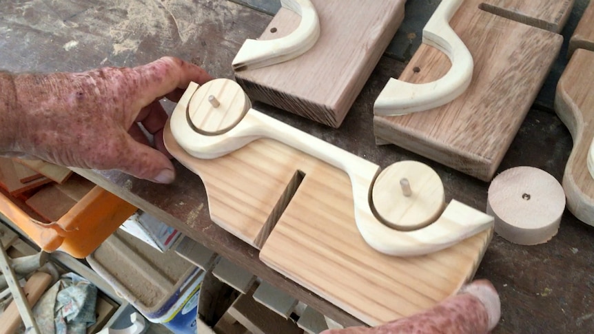 A man holds a wooden toy car that's being constructed.