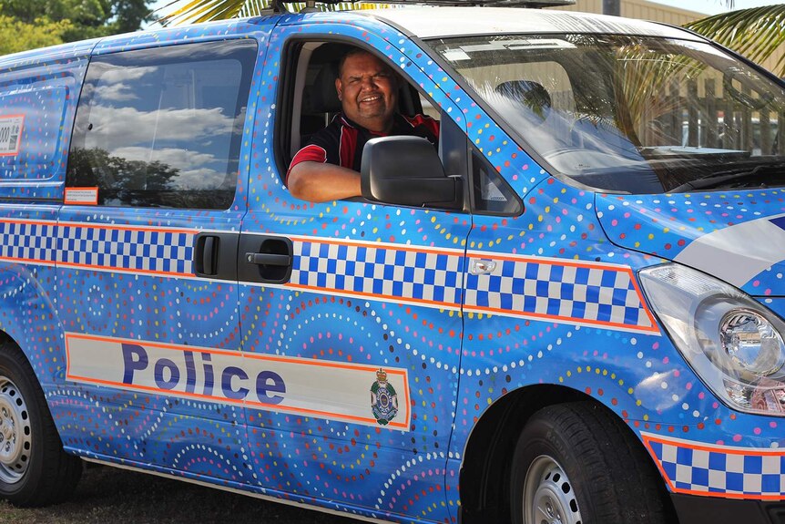 Sam Reuben sits inside a police van painted with Aboriginal art designs.