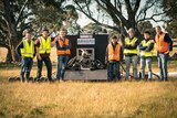 The team of Monash University students standing in a paddock beside their rocket engine launcher.