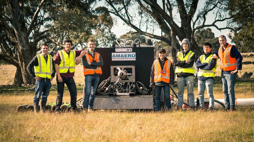 The team of Monash University students standing in a paddock beside their rocket engine launcher.