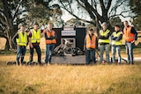 The team of Monash University students standing in a paddock beside their rocket engine launcher.