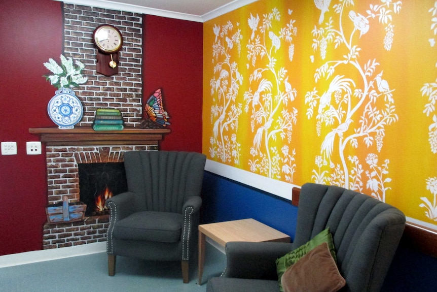 A room with two arm chairs and a mural of a fireplace painted on the wall.
