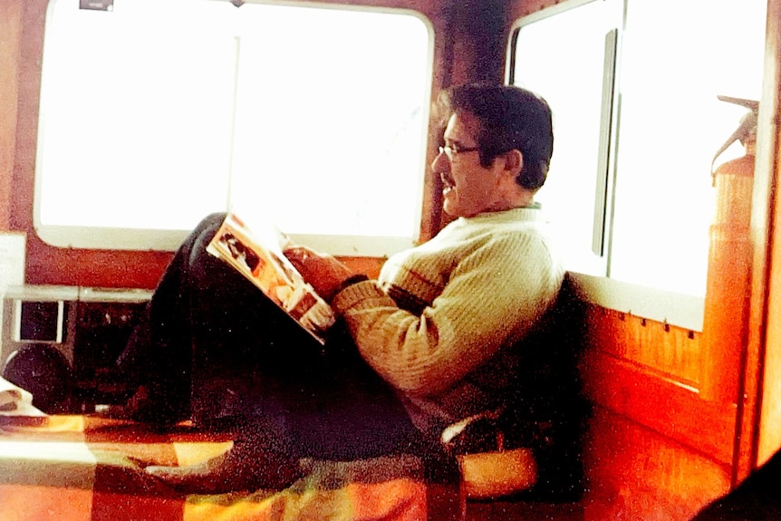 Man sitting stretched out on wooden boat window sill, reading magazine.
