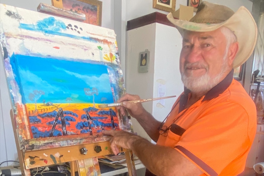  A smiling man wearing a hat and fluro shirt working on a colourful painting 