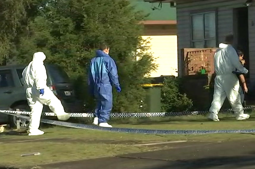 People wearing forensic jumpsuits walk towards a house.