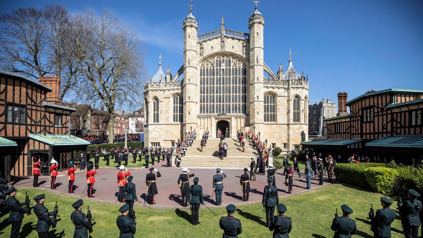 A grand church is surrounded by personell in uniform saluting a coffin entering the steps
