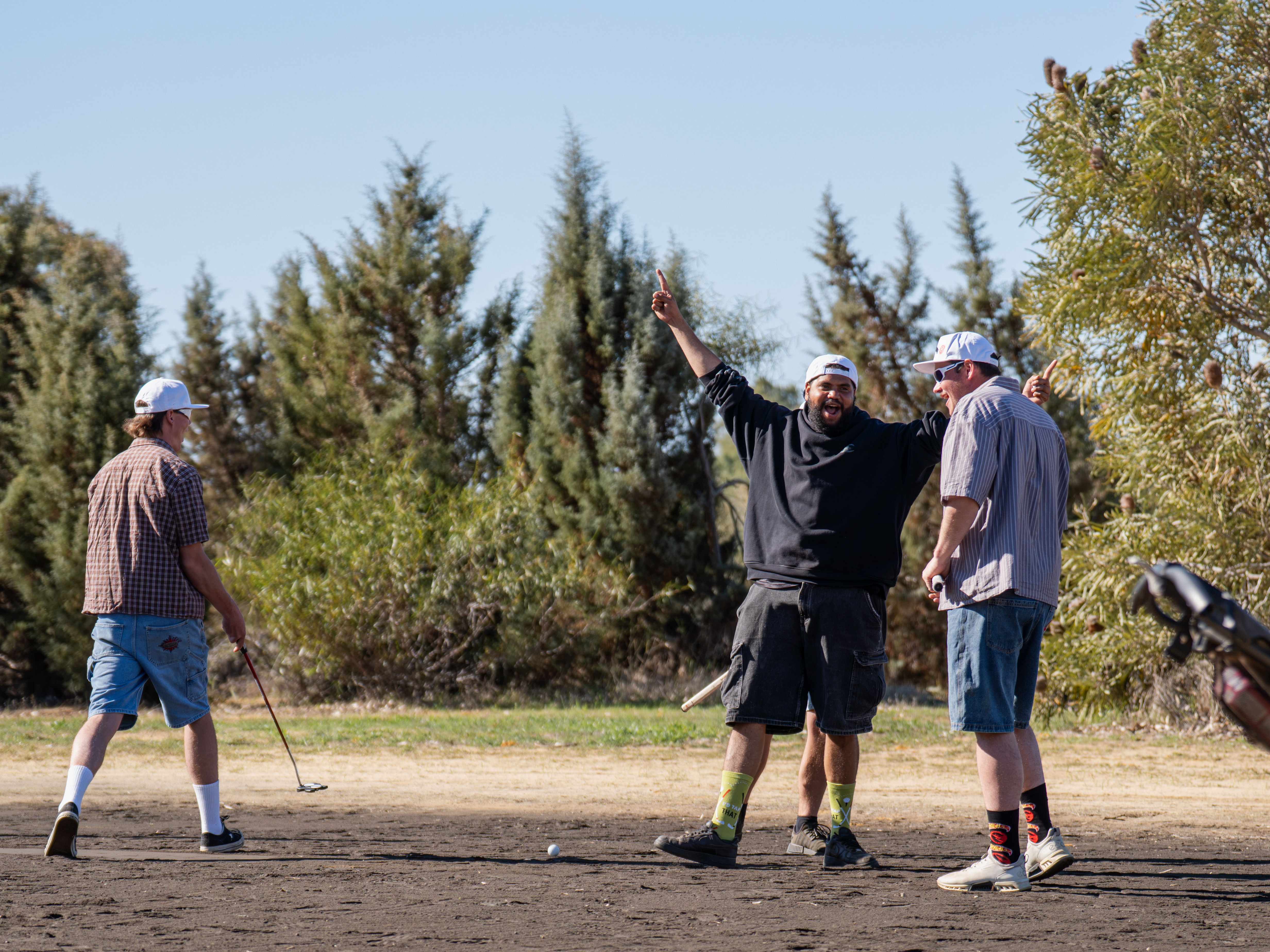 Three young men on a golf course, one has hands in the air celebrating
