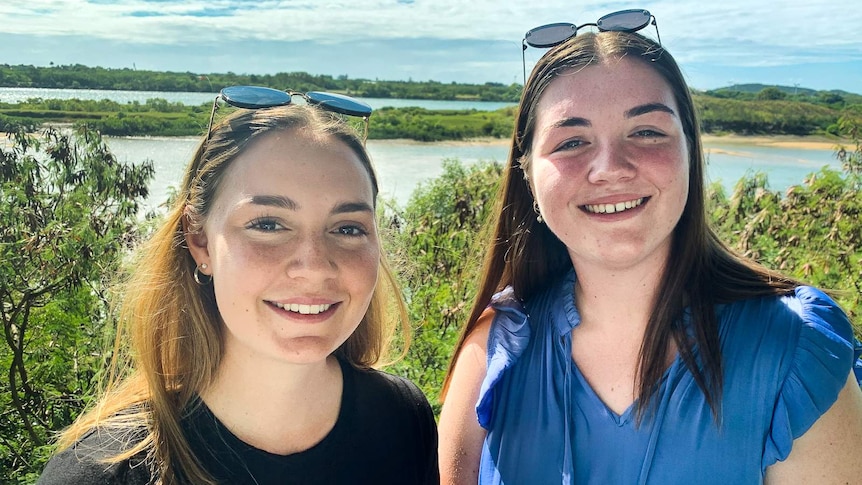 Two young women stand in front of a river