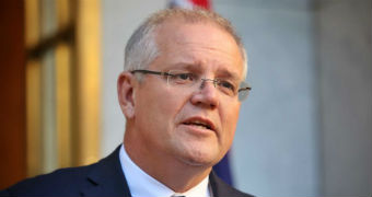 Scott Morrison wears a navy suit and purple tie as he speaks in front of some microphones.