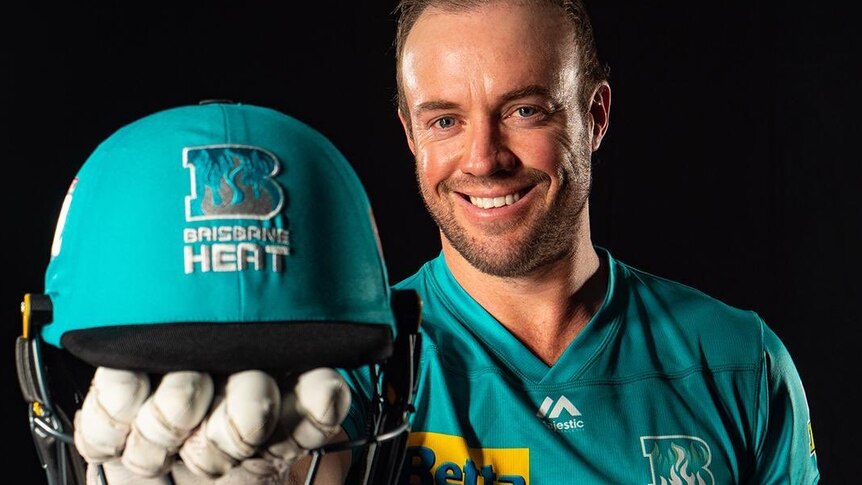 AB de Villiers smiles while holding a Brisbane Heat branded helmet and wearing a Heat jersey.