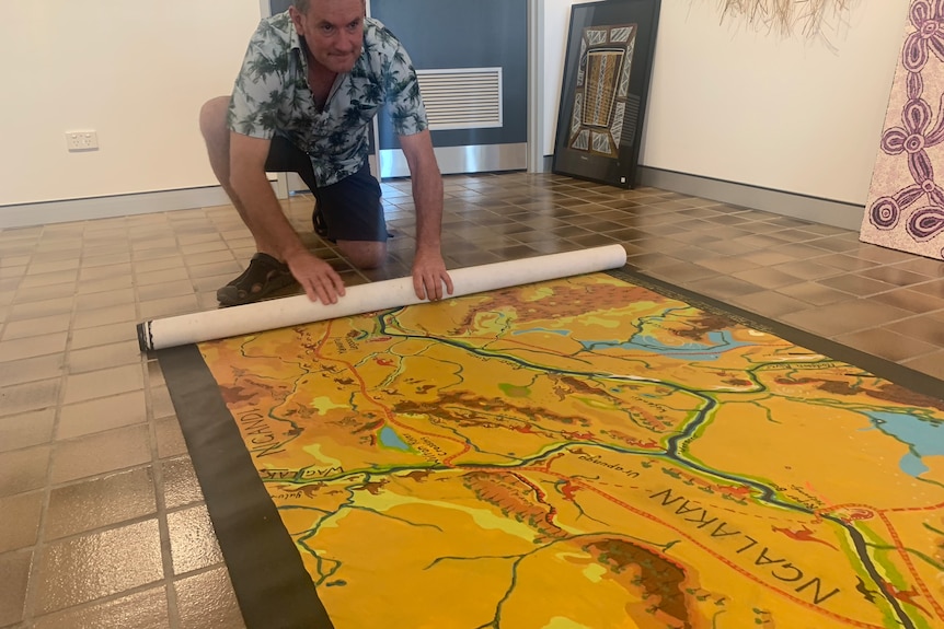 A man crouches on the floor to roll up a large map