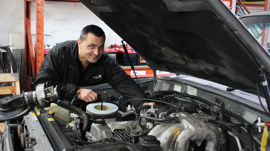 Mechanic Nick Joncevski stands next to an LPG car with its bonnet up.