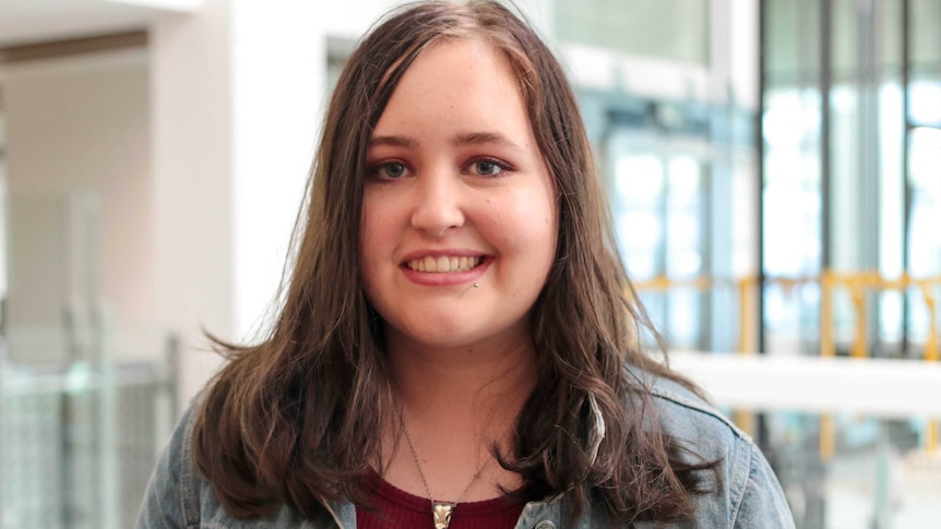 A teenage girl wearing glasses and a white shirt looks at the camera, smiling.