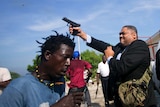 Ralph Fethiere steps out of a car pointing his gun in the air, as protesters scramble
