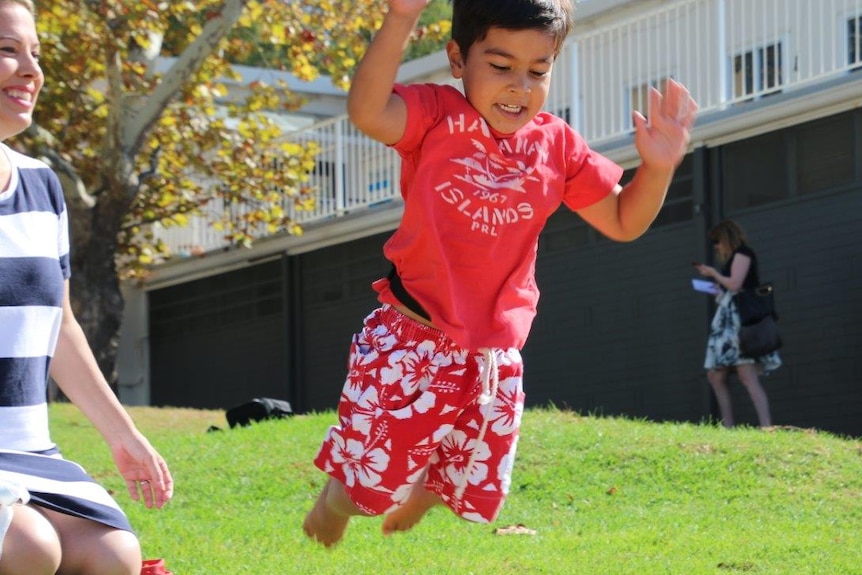 A woman in a black and white striped dress plays with a boy in a red t-shirt and shorts on the grass.