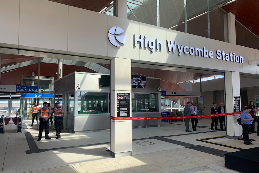 A photo of a train station with a sign that says "High Wycombe Station". Transit guards are standing around. 