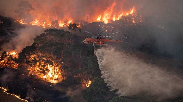 A helicopter travelling over burning bushland.