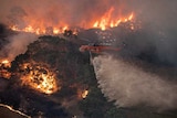 A helicopter travelling over burning bushland.