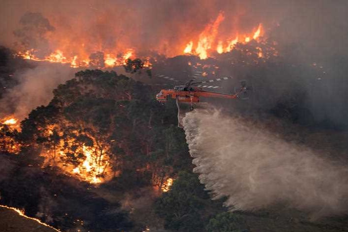 A helicopter travelling over burning bushland.