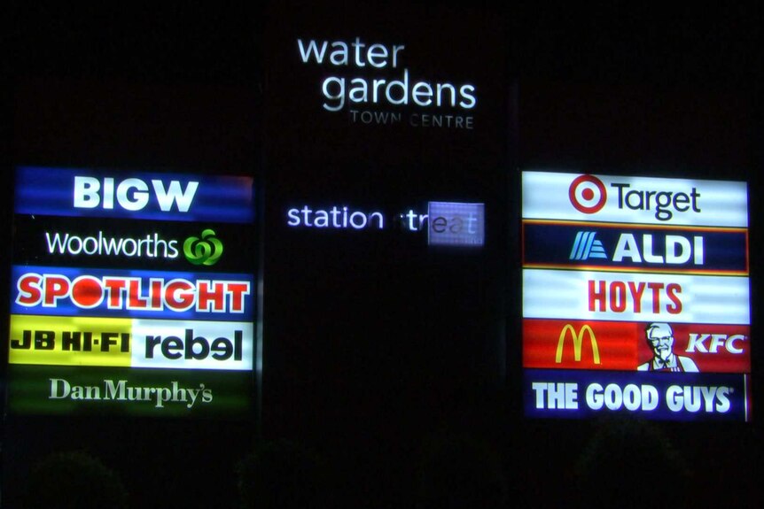 A list of shops outside the Watergardens shopping centre at night.