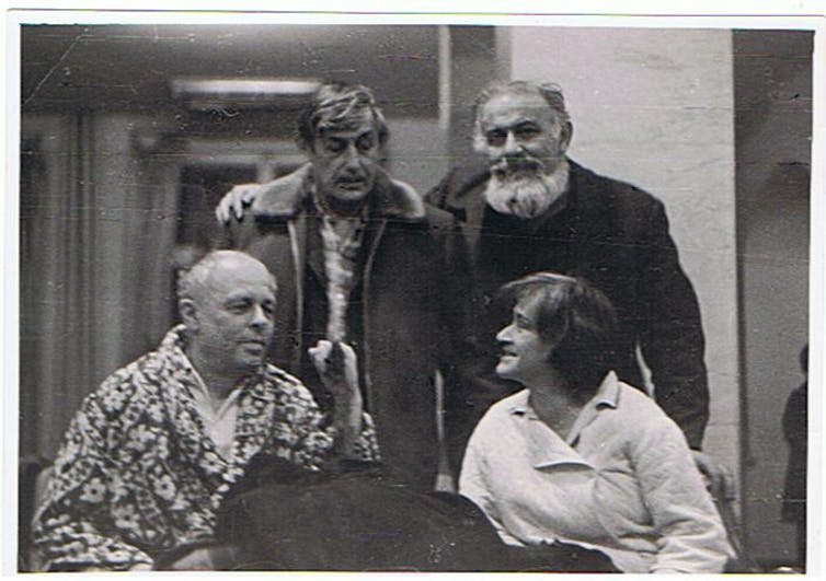 Black and white photograph of four people talking in a room.