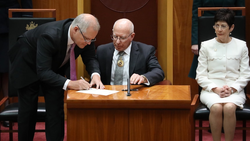 Scott Morrison signs a paper as David Hurley watches on in the senate