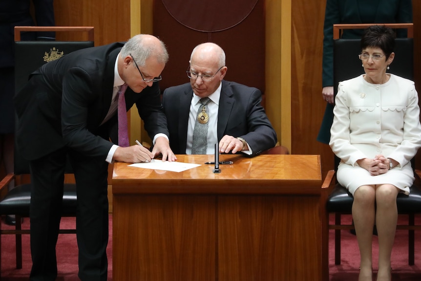Scott Morrison signs a paper as David Hurley watches on in the senate