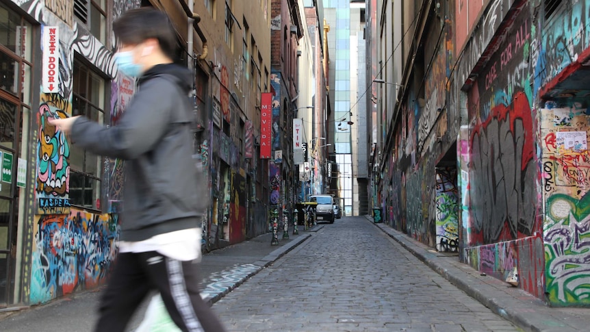 A man wearing a face mask, walking while looking at his phone in Melbourne's CBD.