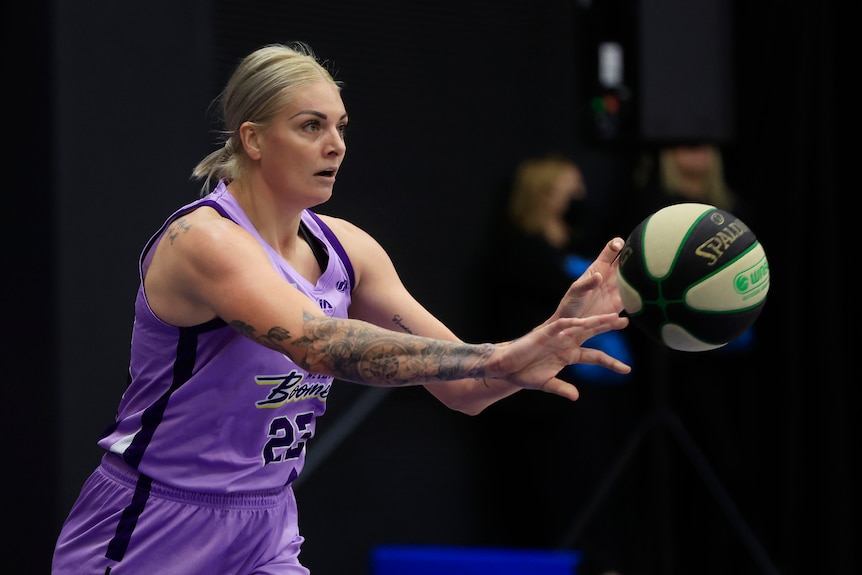 A woman wearing a purple singlet and shorts passes the basketball.