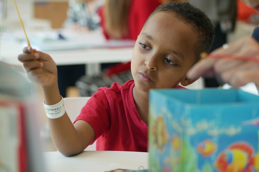 A young boy sits in a hospital classroom playing.