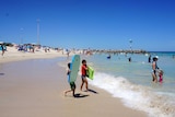 Boys in the foreground with boogie boards enter the water at City Beach.