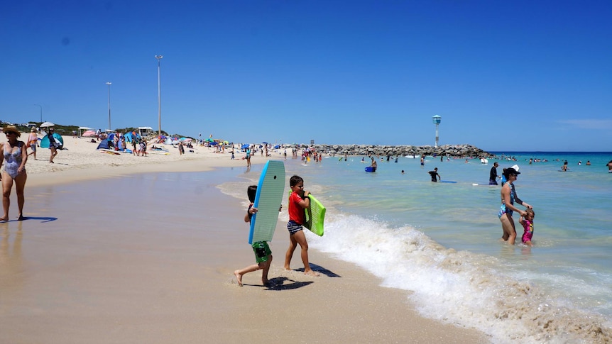 Boys in the foreground with boogie boards enter the water at City Beach.