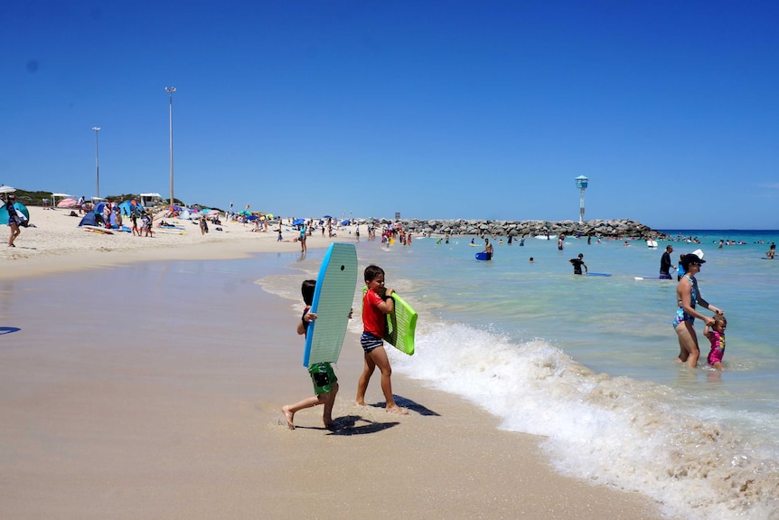 Boys in the foreground with boogie boards enter the water at City Beach.