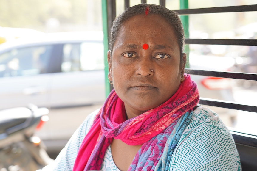 A close up of an Indian woman wearing a pink scarf and blue top with a bindi on her forehand