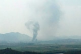 Smoke is seen rising from a distant valley into a cloudy sky.